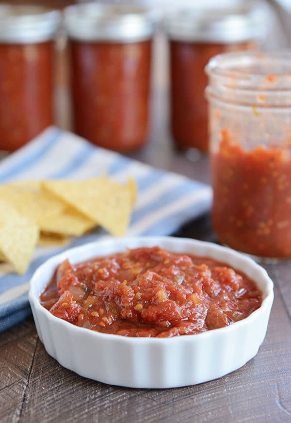 Ramekin of homemade salsa, in front of a half empty jar of salsa and tortilla chips.