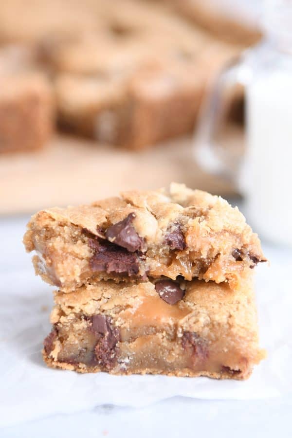 Two salted caramel brown butter chocolate chip bars stacked on each other on white wax paper.