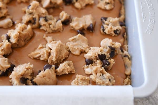 Process shot of chocolate chip cookie dough dotting surface of caramel.