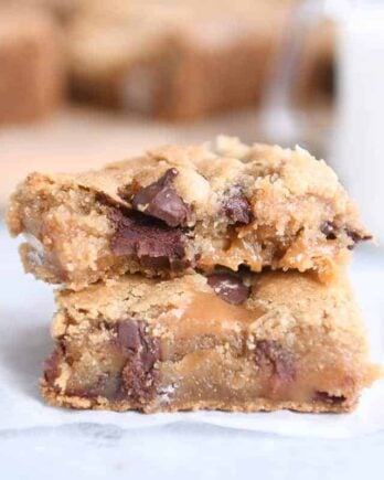 Two salted caramel brown butter chocolate chip bars stacked on each other on white wax paper.