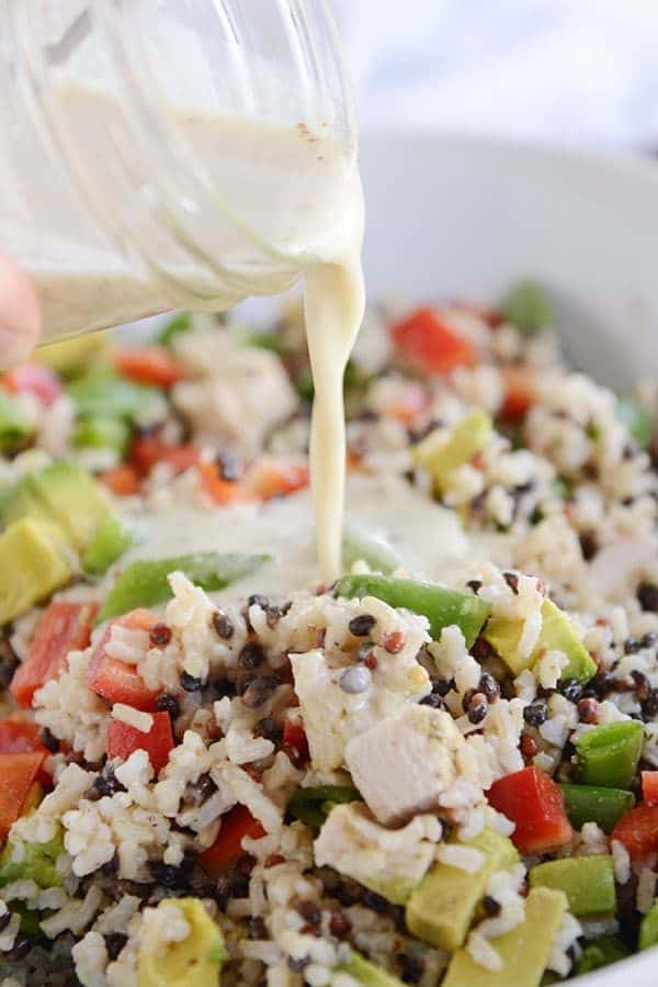 Dressing getting poured over a bowl of santa rosa chicken and wild rice salad.