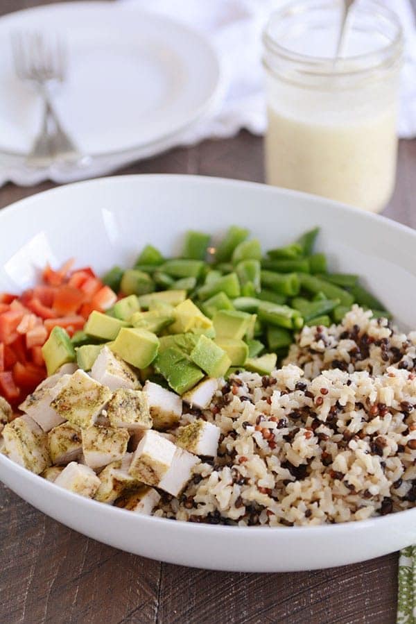 A large white bowl of cooked wild rice, chopped chicken, diced avocado, red pepper, and green beans.