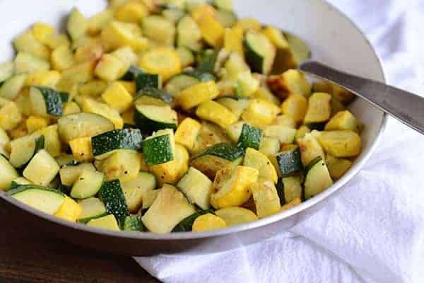 A skillet full of sautéed zucchini and yellow squash, with a full spoonful of the saute on top of the mixture.