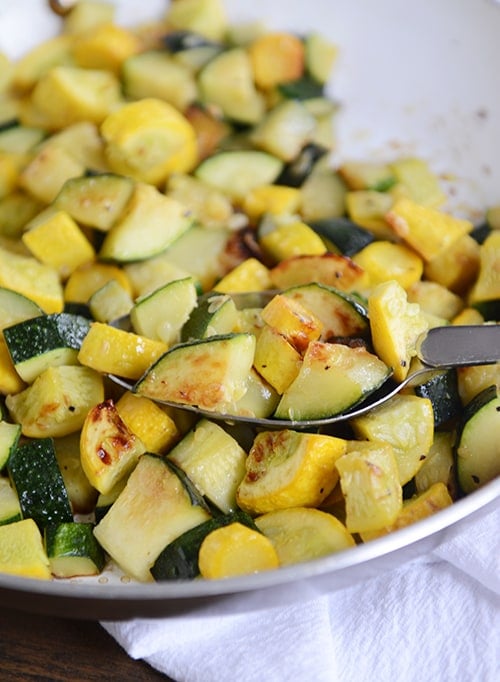 A plate full of sautéed zucchini and yellow squash, with a full spoonful of the saute on top of the mixture. 