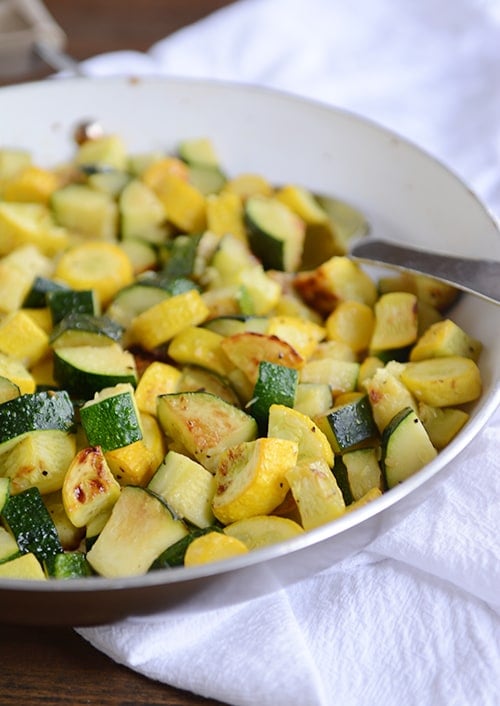 A skillet full of sautéed zucchini and yellow squash, with a full spoonful of the saute on top of the mixture.