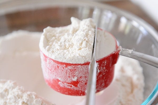 A butter knife leveling off a measuring cup full of flour. 