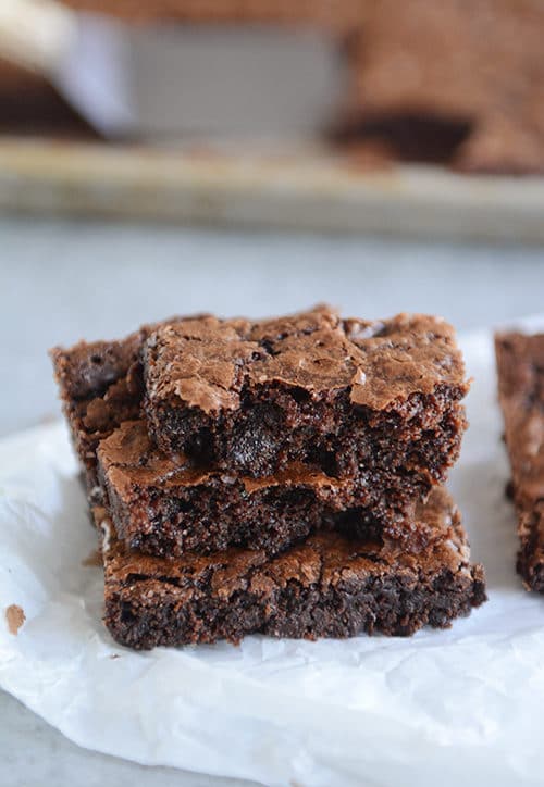 Chocolate brownies stacked on top of each other on a piece of parchment.