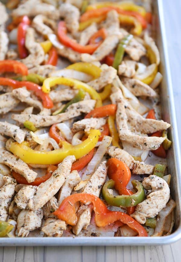 Sheet pan loaded with bell peppers and chicken strips for easy sheet pan chicken fajitas.