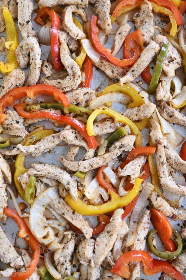 Sheet pan loaded with bell peppers and chicken strips for easy sheet pan chicken fajitas.