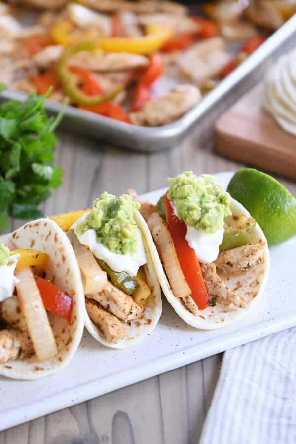 Three easy sheet pan chicken fajitas on white board topped with sour cream and guacamole.