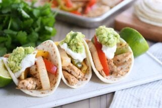 Three easy sheet pan chicken fajitas on white board topped with sour cream and guacamole.