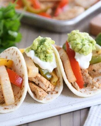 Three easy sheet pan chicken fajitas on white board topped with sour cream and guacamole.