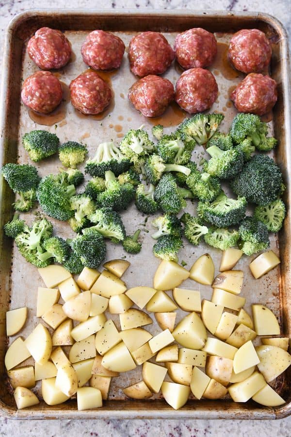 Top down view of sheet pan with uncooked meatballs, broccoli and potatoes.