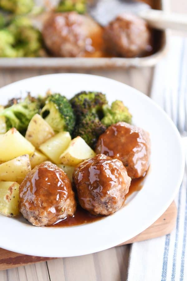 White plate filled with meatballs drizzled in sweet and sour sauce and roasted vegetables.