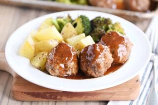 White plate filled with meatballs drizzled in sweet and sour sauce and roasted vegetables.