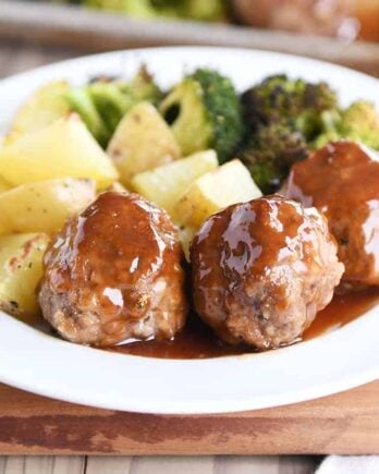 White plate filled with meatballs drizzled in sweet and sour sauce and roasted vegetables.