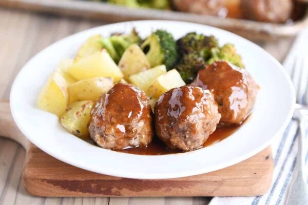 White plate filled with meatballs drizzled in sweet and sour sauce and roasted vegetables.