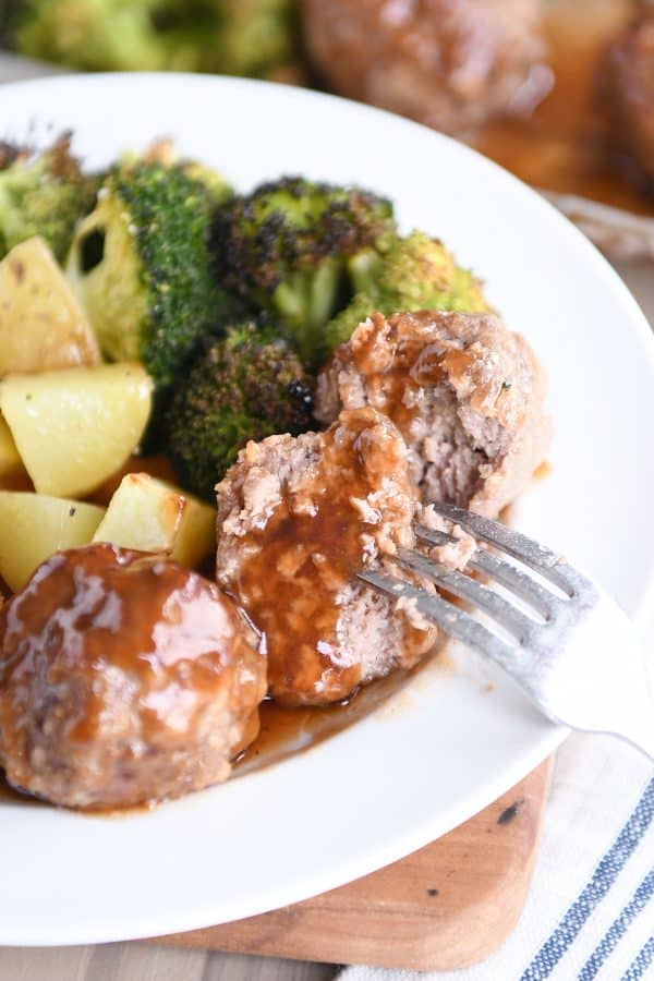 Fork piercing half of a sweet and sour sheet pan meatball on white plate.