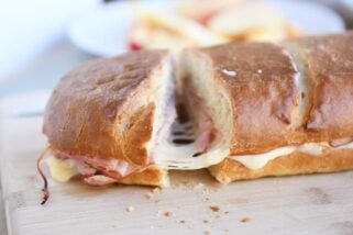 Cutting a slice of ham and cheese sheet pan panini on wood cutting board.