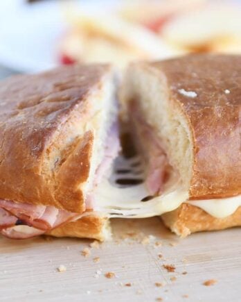 Cutting a slice of ham and cheese sheet pan panini on wood cutting board.