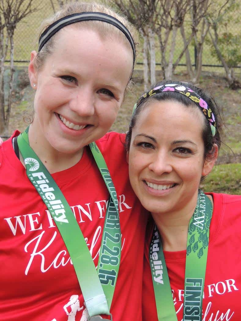 Two woman with race medals around their neck. 