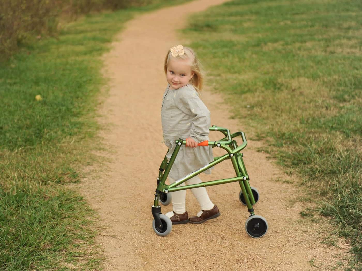 A little girl using a walker on a dirt path. 