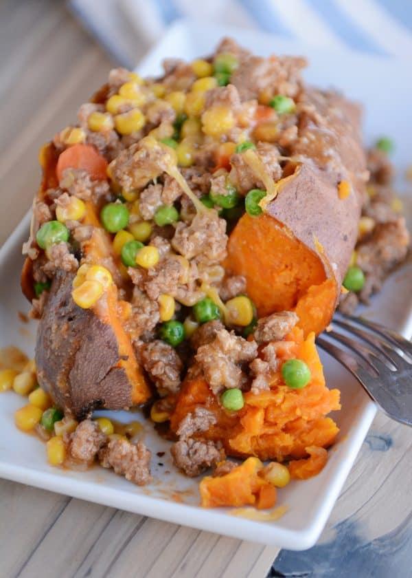 A sweet potato with shepherd's pie filling on top on a white plate. 