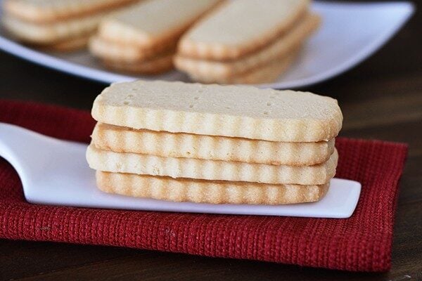 A stack of four shortbread cookies with more cookies on a plate behind them.