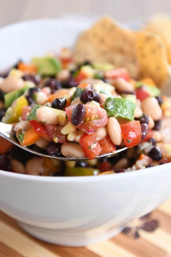 A metal spoon taking a helping of cowboy caviar dip out of a white bowl.