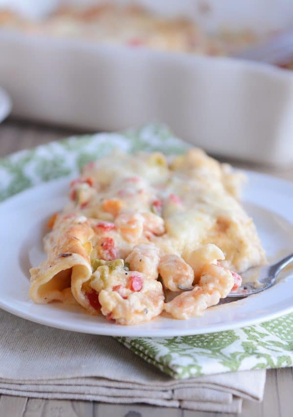 Taking a bite out of a shrimp enchilada on a white plate.