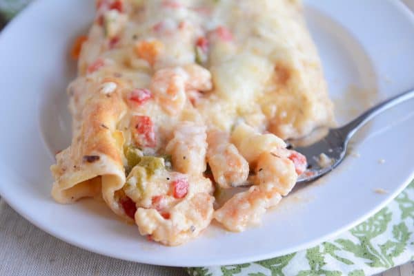 Closeup of taking a bite out of a shrimp enchilada on a white plate.