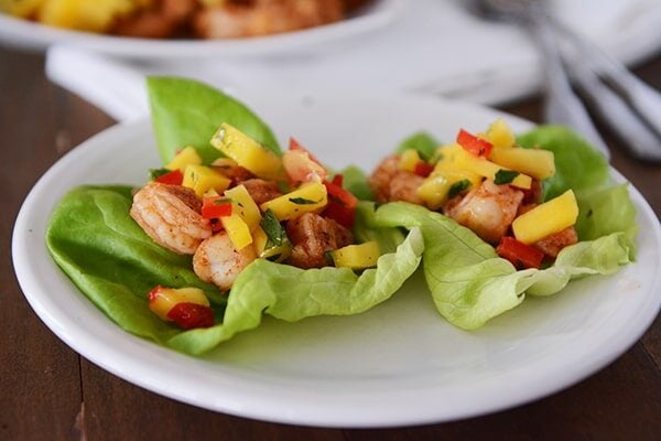 Two shrimp and mango lettuce wraps next to each other on a white plate.