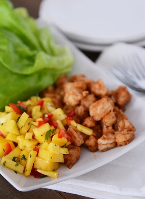 A white platter with cooked shrimp on one side and chopped mango salsa on the other side.