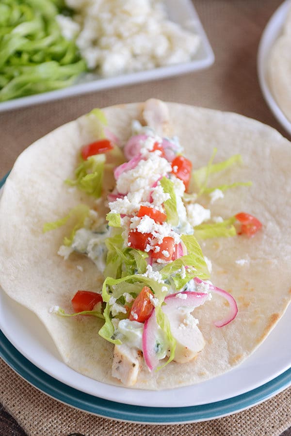 A tortilla filled with chicken, lettuce, onion, tomato, and feta. 