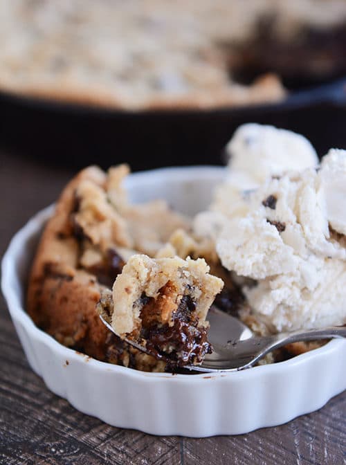 A white ramekin with a a chocolate chip cookie dessert next to a scoop of ice cream.