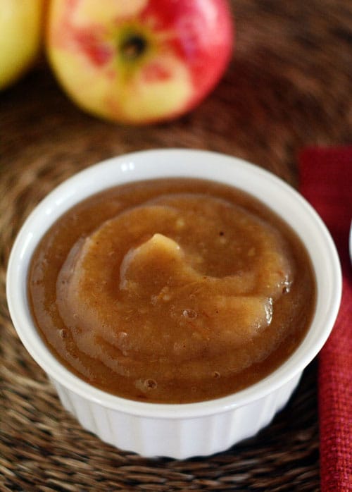 Top view of a white ramekin of applesauce with a fresh apple behind it. 
