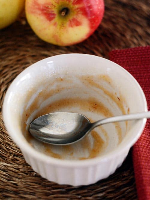 A white ramekin with a spoon and a little bit of applesauce left in it.