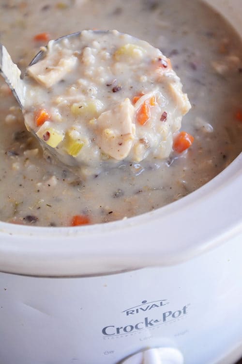 A ladle taking a big scoop of creamy chicken soup out of a crockpot.