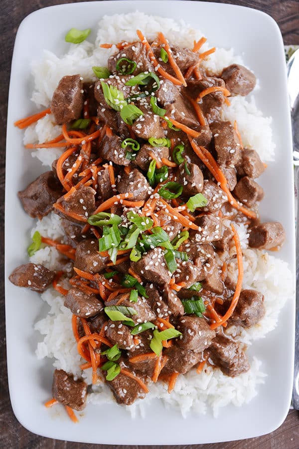 A plate full of white rice topped with cubes of beef, shredded carrots, and green onions.