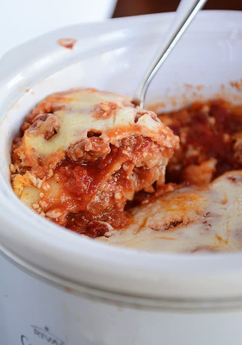 A spoon taking a helping of lasagna out of a slow cooker. 