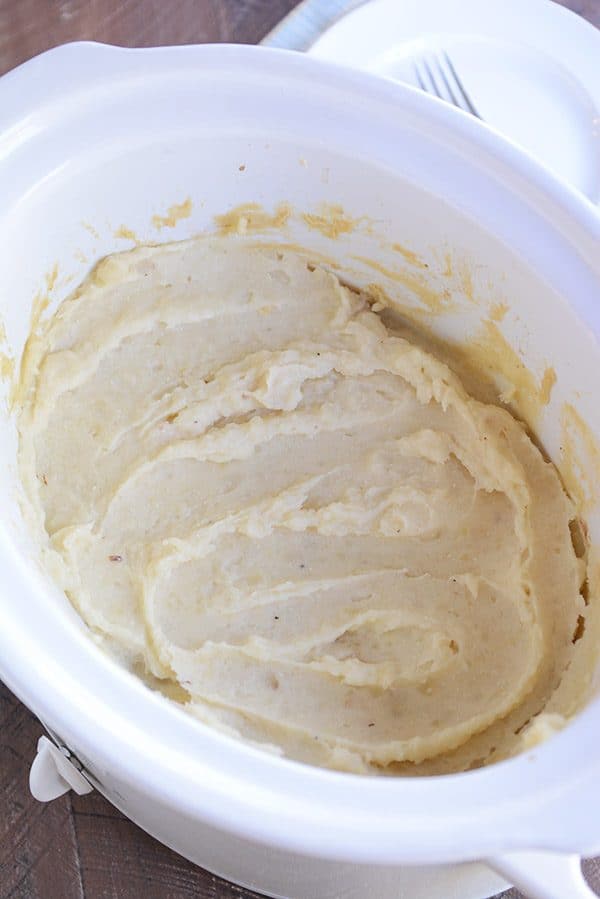 A white crockpot full of creamy mashed potatoes.