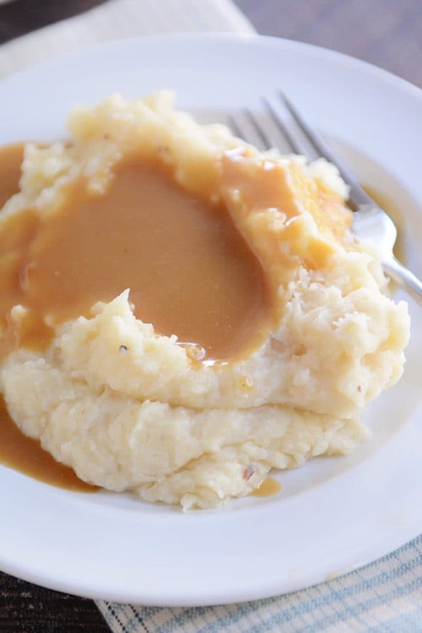 A white plate with a large serving of mashed potatoes covered in brown gravy.