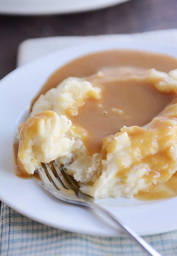 Mashed potatoes covered in brown gravy on a white plate.