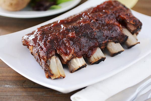 A rack of ribs topped with sauce on a white platter. 