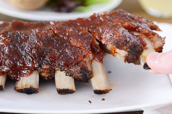 Two ribs being pulled off a cooked rack of ribs. 
