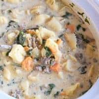 Slow cooker full of slow cooker tortellini sausage potato spinach soup with ladle scooping soup.