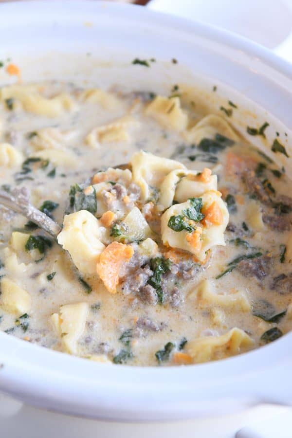 Slow cooker full of slow cooker tortellini sausage potato spinach soup with ladle scooping soup.