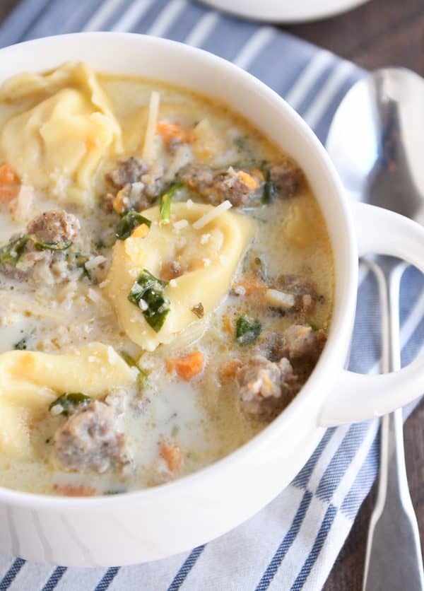 Close up of white bowl with slow cooker tortellini sausage spinach soup.