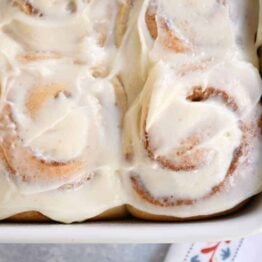 Small batch cinnamon roll recipe with dough baked and frosted in white pan.