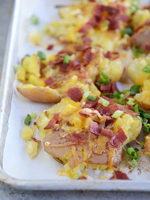 A cookie sheet full of bacon and cheese topped potatoes.